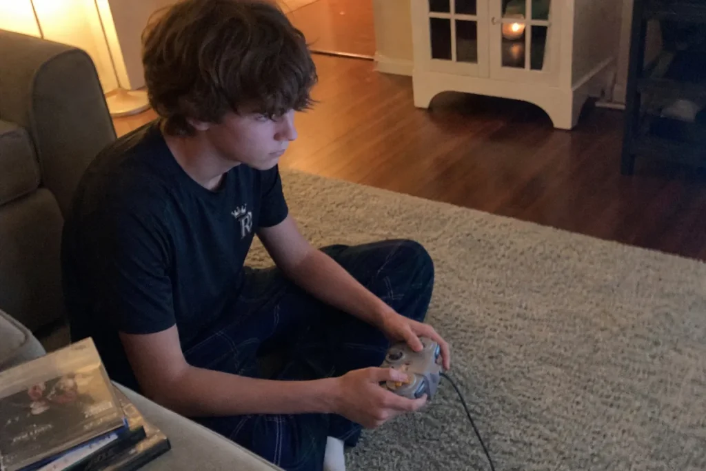 En tonåring sitter på golvet med en handkontroll och spelar, troligen inspirerad av Golden Axe remake.