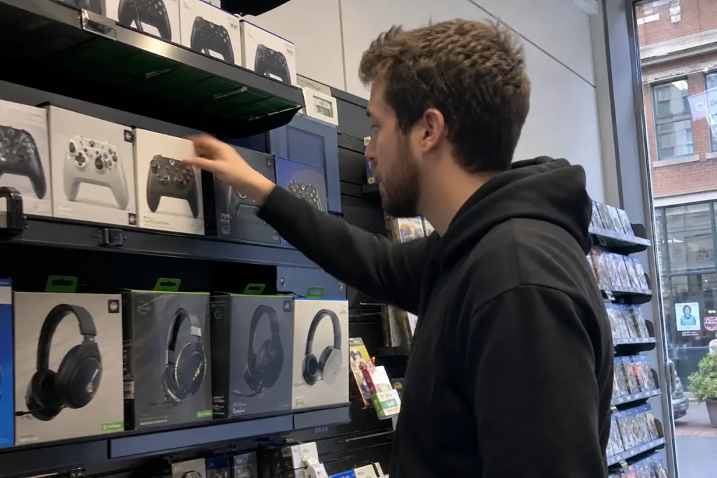 Ung man i luvtröja sträcker sig efter en spelkontroll i en butikshylla med Warlock Dungeons Dragons spel