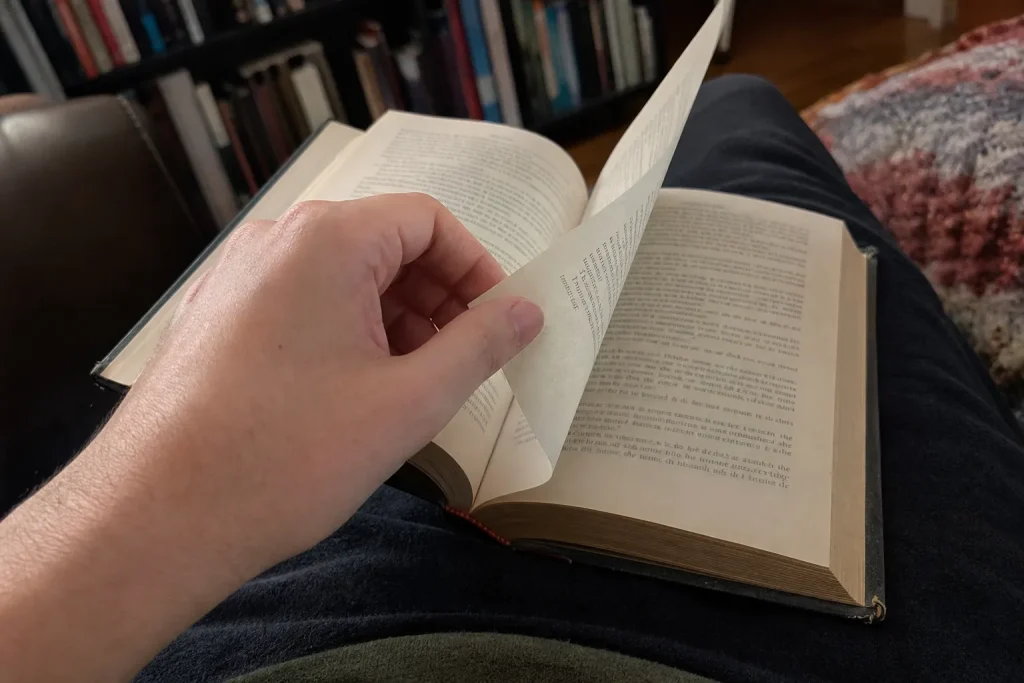 Hand bläddrar i inbunden fantasybok i soffan, en stunds läsning inför Hogwarts Legacy uppföljare.