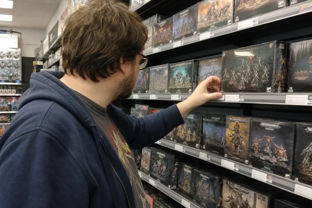 Kund i spelbutik plockar upp en miniatyrfigursbox, möjligen kopplad till Total War Warhammer 40000.