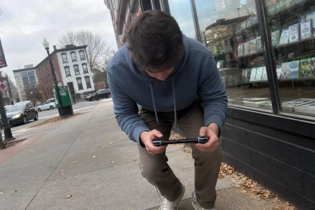 En kille böjer sig ner och tittar på sin handhållna spelkonsol utanför ett spelbutiksfönster, i samband med Halloween: The...