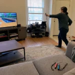 En person spelar Nintendo Switch Sports Resort med en Joy-Con i vardagsrummet framför TV:n.