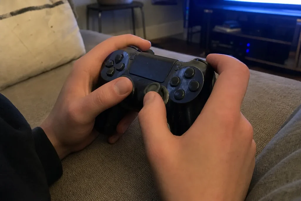 Närbild på händer som håller i en handkontroll framför tv:n, troligen mitt i ett parti av State of Decay 3.